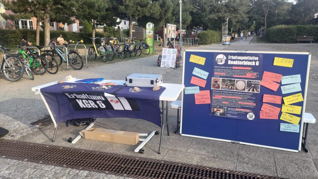 Der Diskussionsstand in Lubmin. Ein Tisch mit Flyern und dem Initiativen-Logo auf einem Banner. Daneben steht eine Pinnwand mit einem Info-Plakat und Ideen auf Notizzetteln.