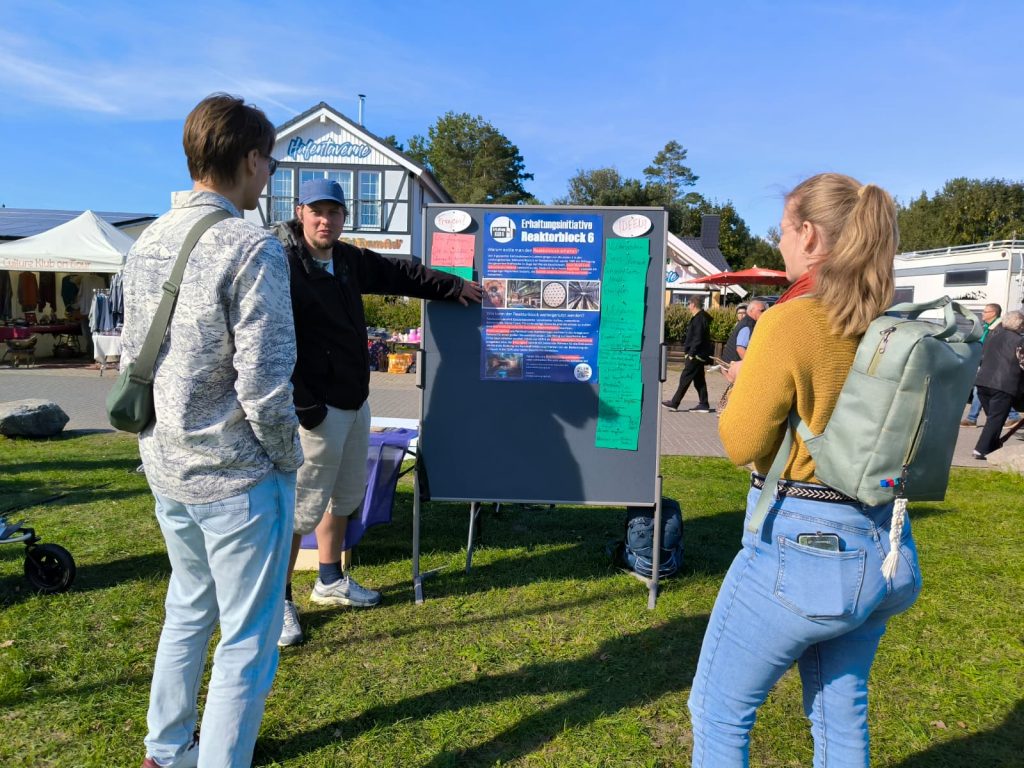 Am Diskussionsstand wird 2 Personen anhand eines Plakats die Bedeutung des KGR 6 erklärt.